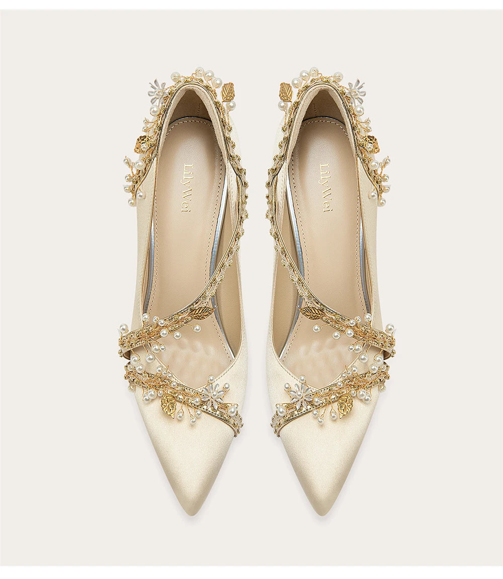 Pair of white high-heeled shoes with gold embellishments on a light background