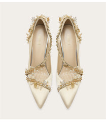 Pair of white high-heeled shoes with gold embellishments on a light background