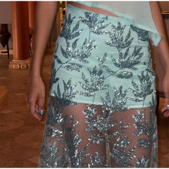 Close-up of a person wearing a light blue sequin skirt with a floral pattern.