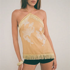 Woman wearing a yellow halter top with floral design and fringe details on a plain background