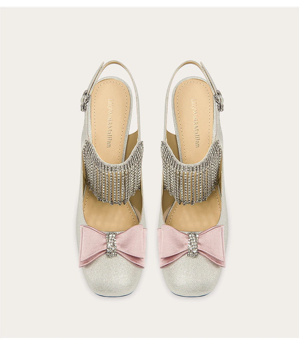 Silver high-heeled sandals with pink bows and rhinestone embellishments on a light gray background