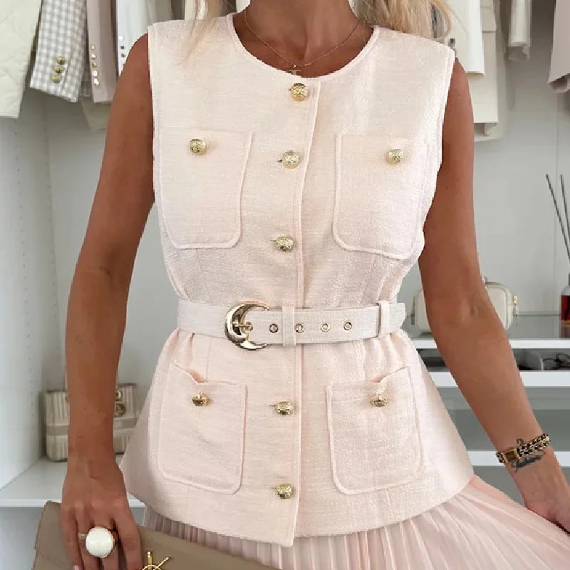 Woman wearing a light pink sleeveless jacket with gold buttons in a store setting.