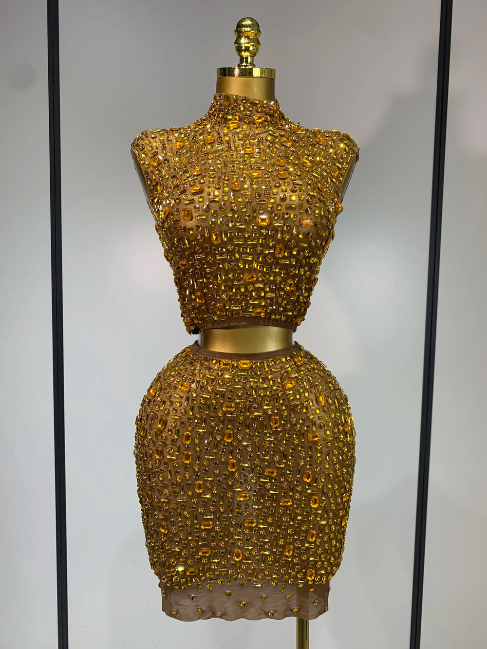 Gold beaded dress form against a neutral background