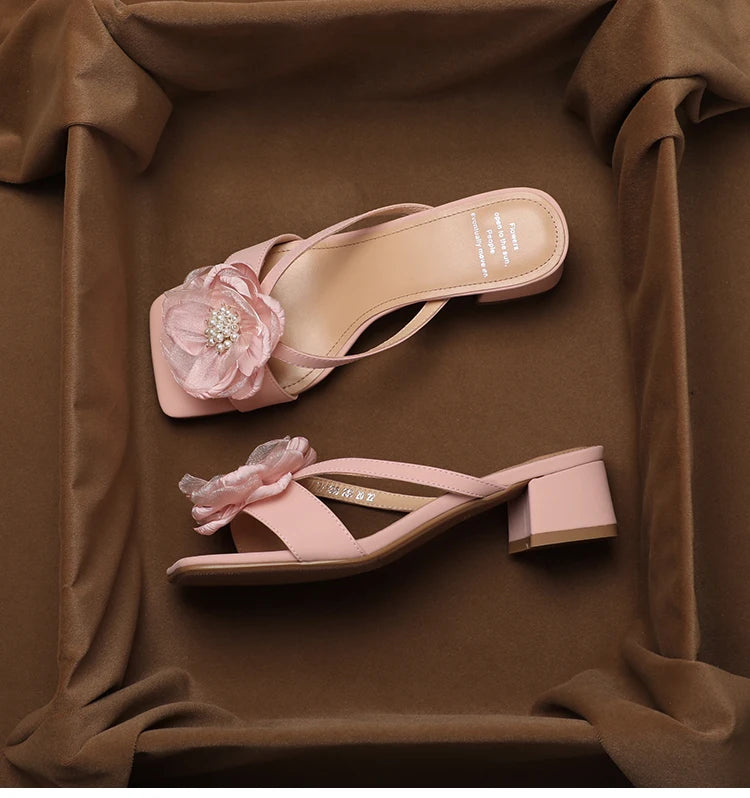 Pair of pink sandals with floral decorations on a brown fabric background