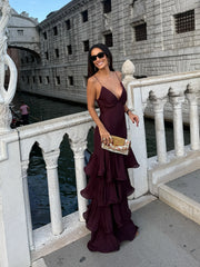 Woman in a burgundy dress standing on a bridge over a canal with historic buildings in the background.
