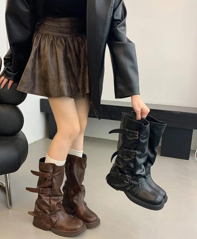 Person wearing brown leather boots and holding black boots indoors.