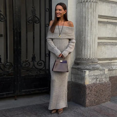 Woman in a gray off-shoulder sweater and long skirt standing in front of classical architecture.