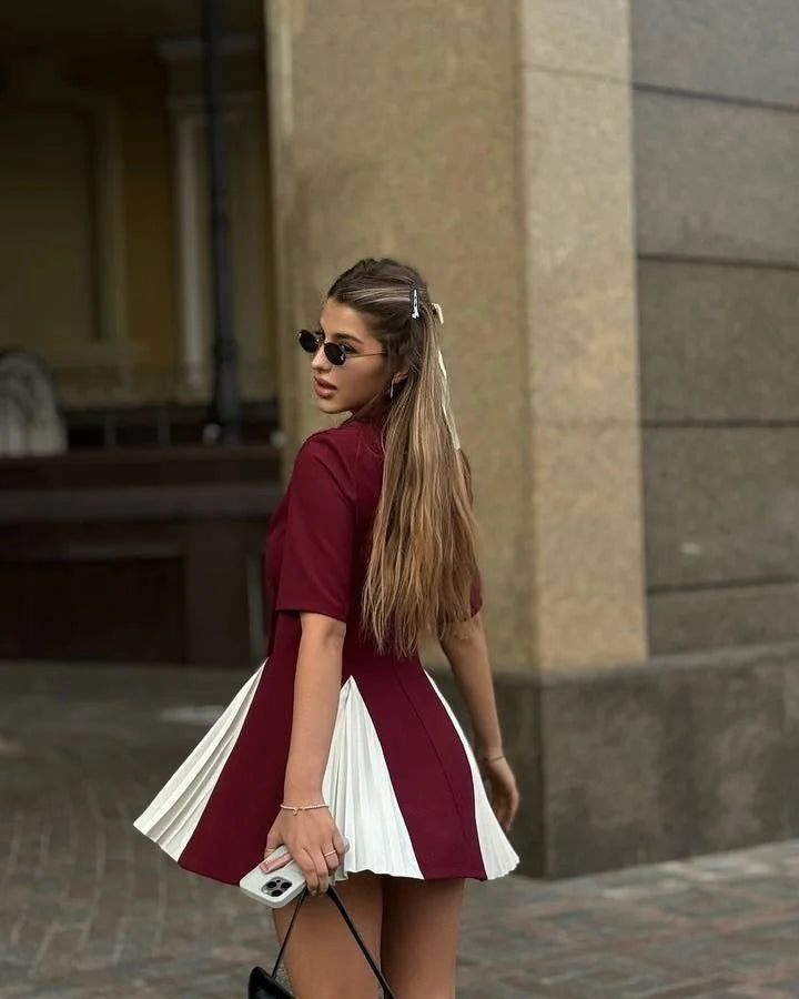 Woman in a red and white dress standing against a stone wall.