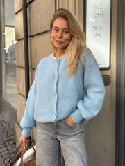 Woman wearing a light blue sweater and jeans standing against a building.