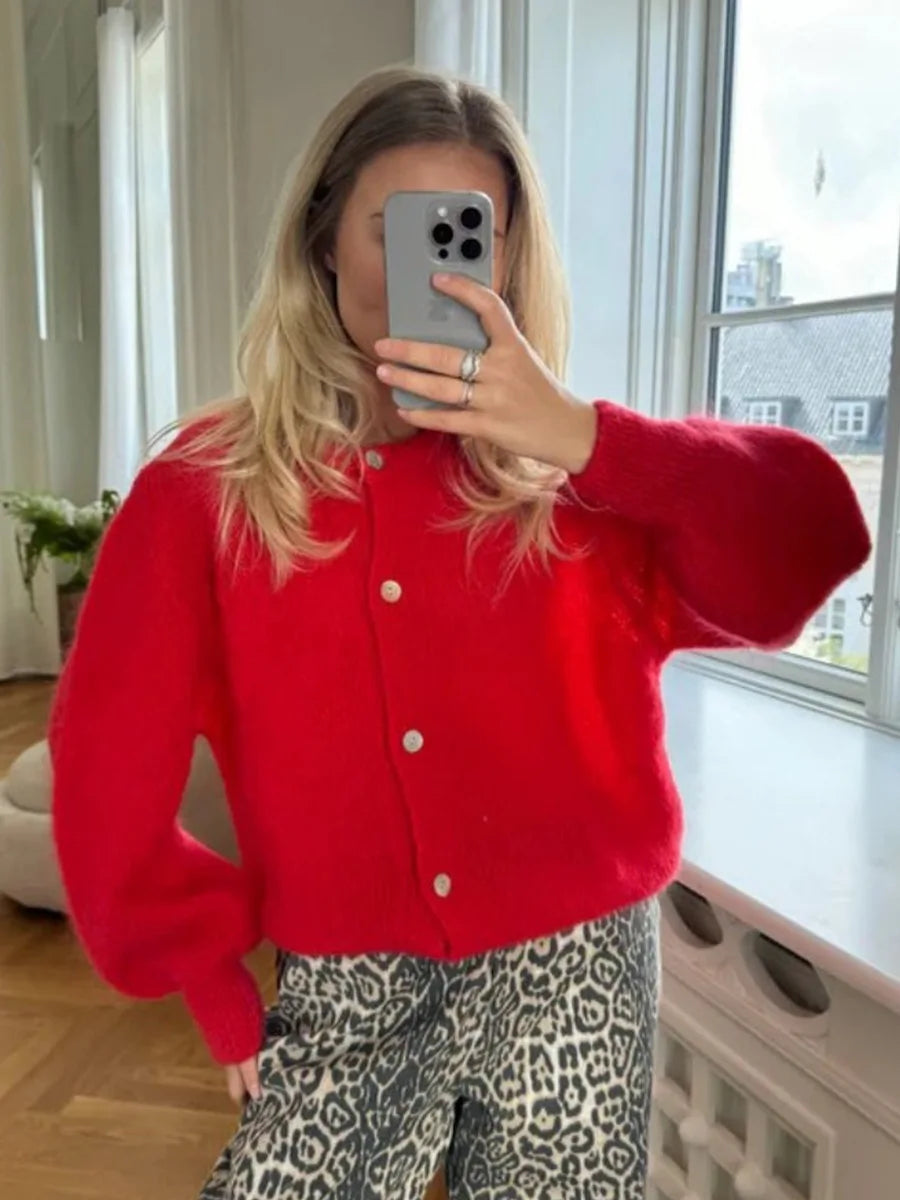 Person wearing a red cardigan and patterned pants taking a mirror selfie.