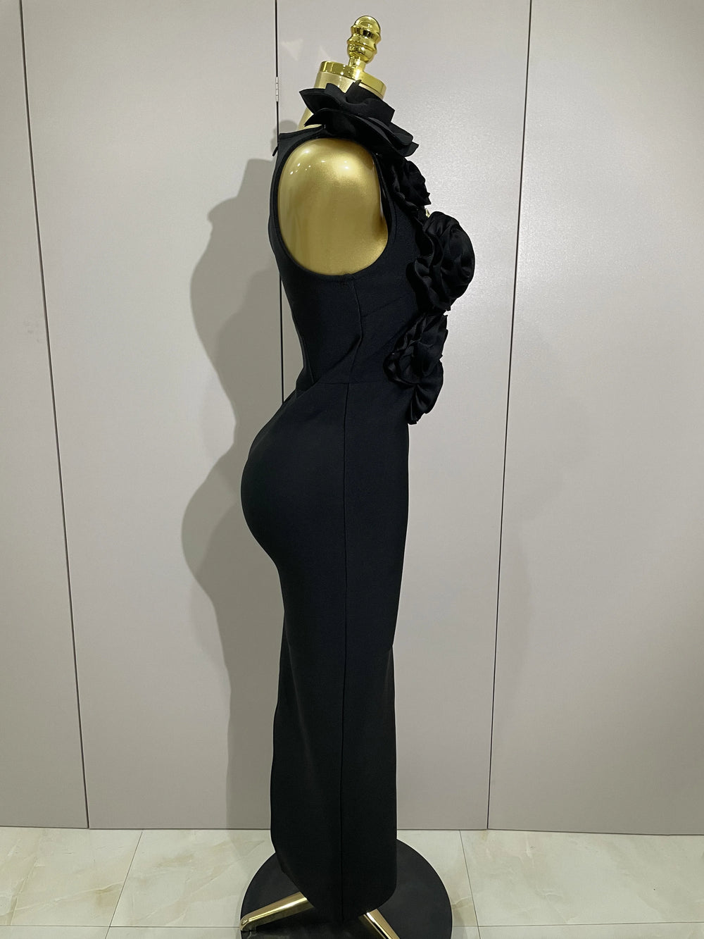 Black evening gown on a mannequin with a gold head against a white wall.