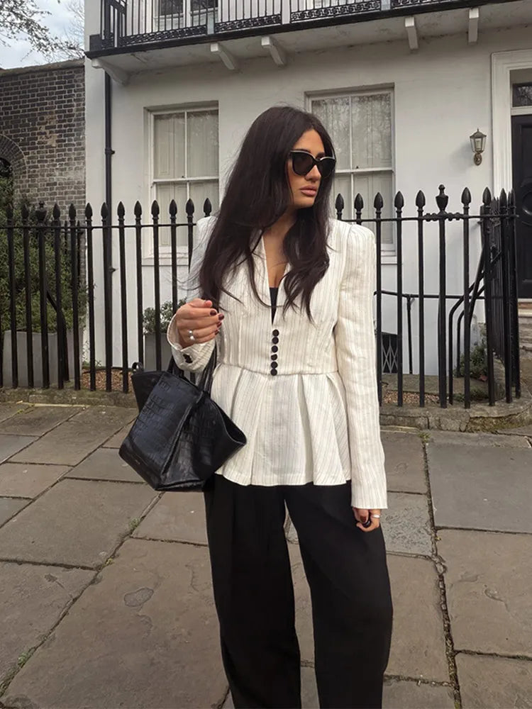 A woman in a white top and black pants is standing on a sidewalk with a building in the background.