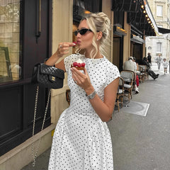 Woman in a polka dot dress eating ice cream on a city street.
