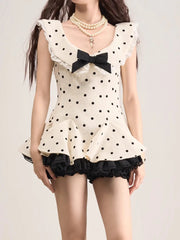 Woman wearing a polka dot top with a bow and black shorts on a plain background