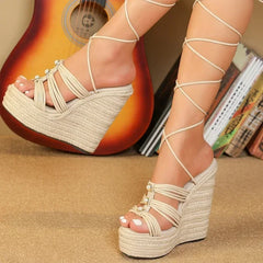 Beige wedge sandals with strappy design worn by a person, with a guitar and books in the background.