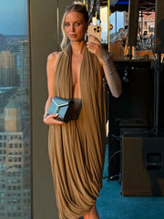 Woman in a flowing beige dress taking a selfie in an urban setting with cityscape in the background.