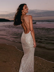 Woman in a sparkly dress standing on a beach at sunset