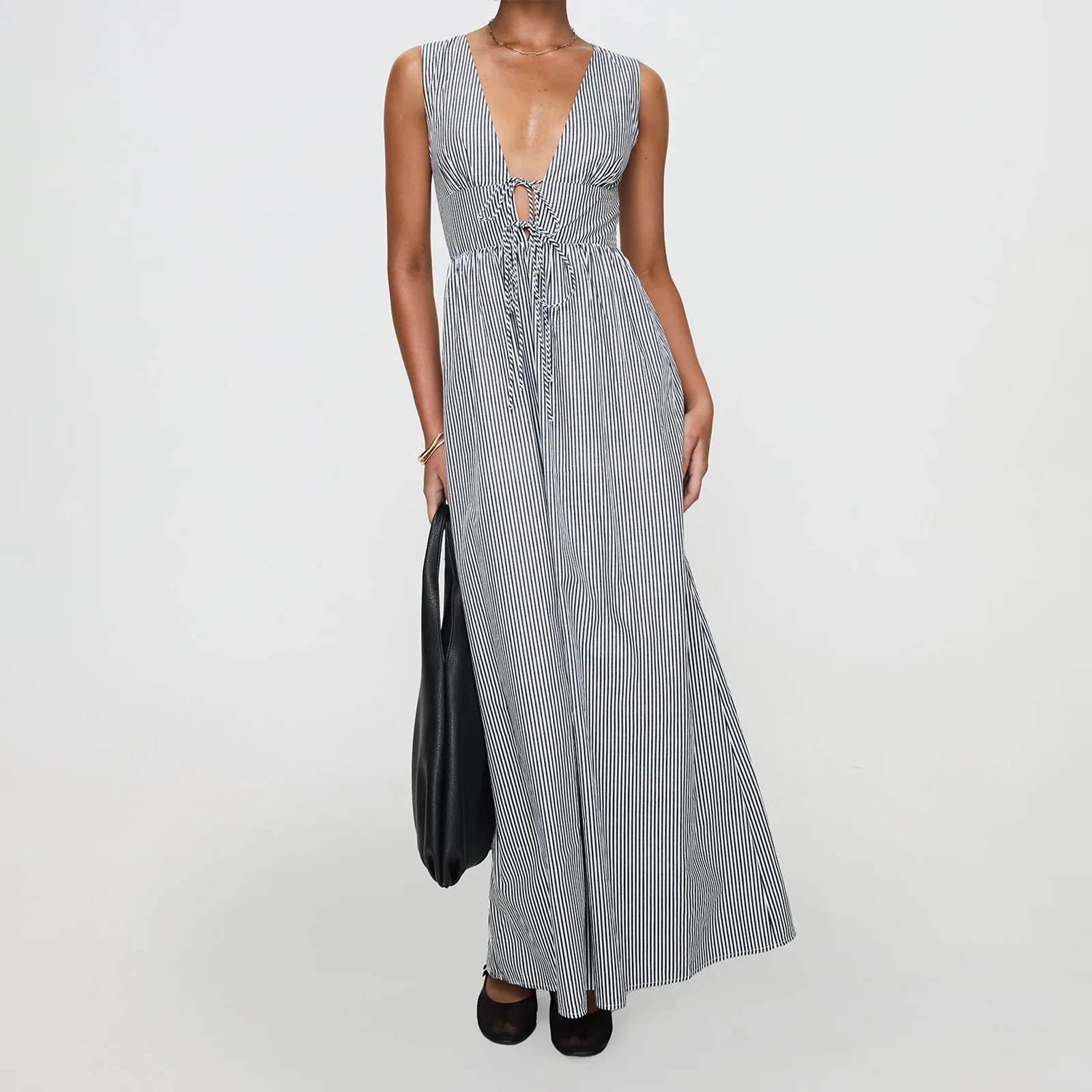 Woman wearing a long striped dress holding a black bag on a white background