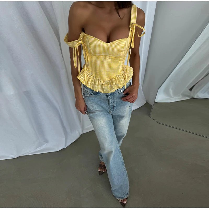 Person wearing a yellow checkered top and blue jeans against a white curtain background