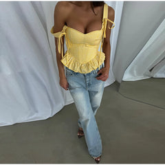 Person wearing a yellow checkered top and blue jeans against a white curtain background