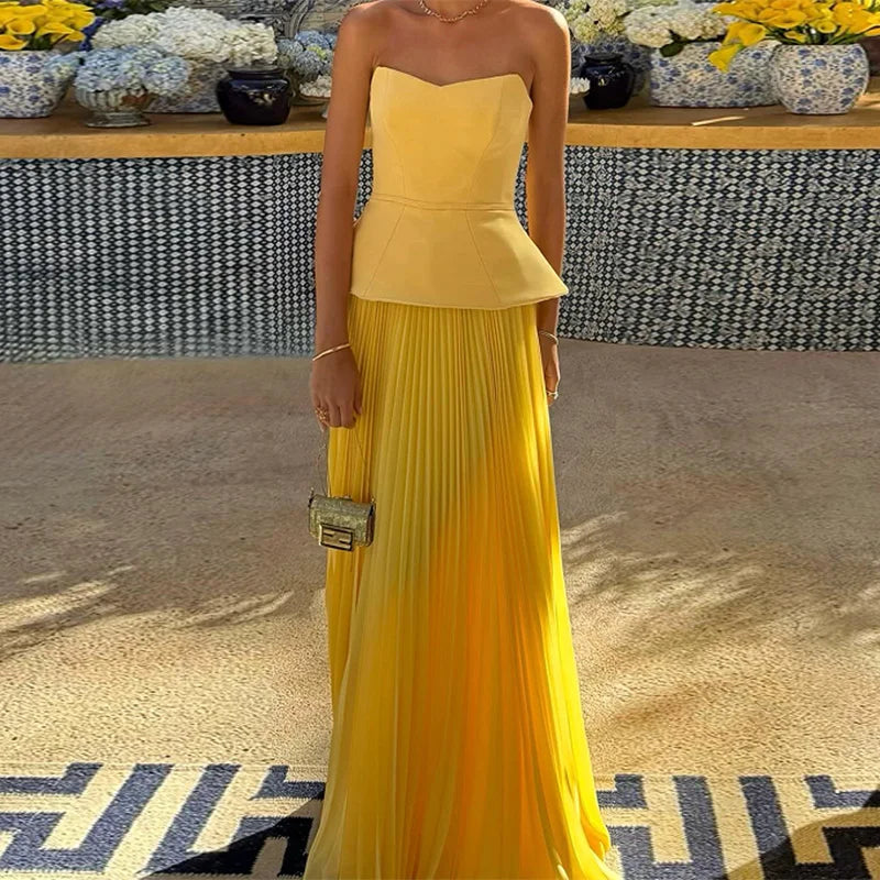 Woman wearing a yellow strapless dress with a pleated skirt, standing indoors.