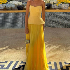 Woman wearing a yellow strapless dress with a pleated skirt, standing indoors.