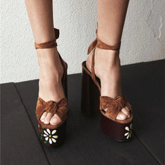 Brown suede platform sandals with floral designs on a dark surface.
