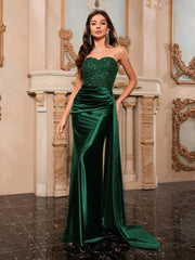 Woman in a green evening gown standing in an elegant interior setting.