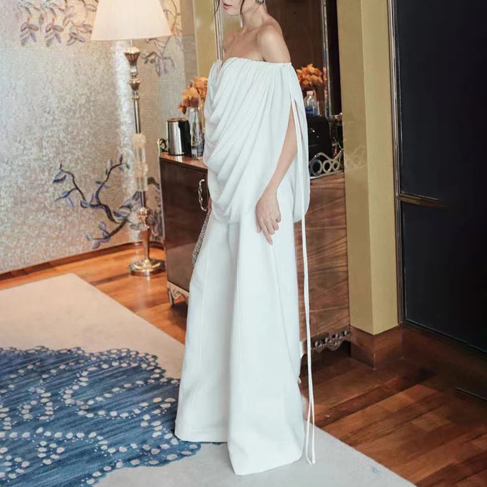 Woman in a white saree standing in a room with wooden flooring and decorative elements.