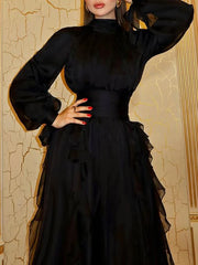 Woman wearing a black dress with sheer sleeves against a decorative wall.