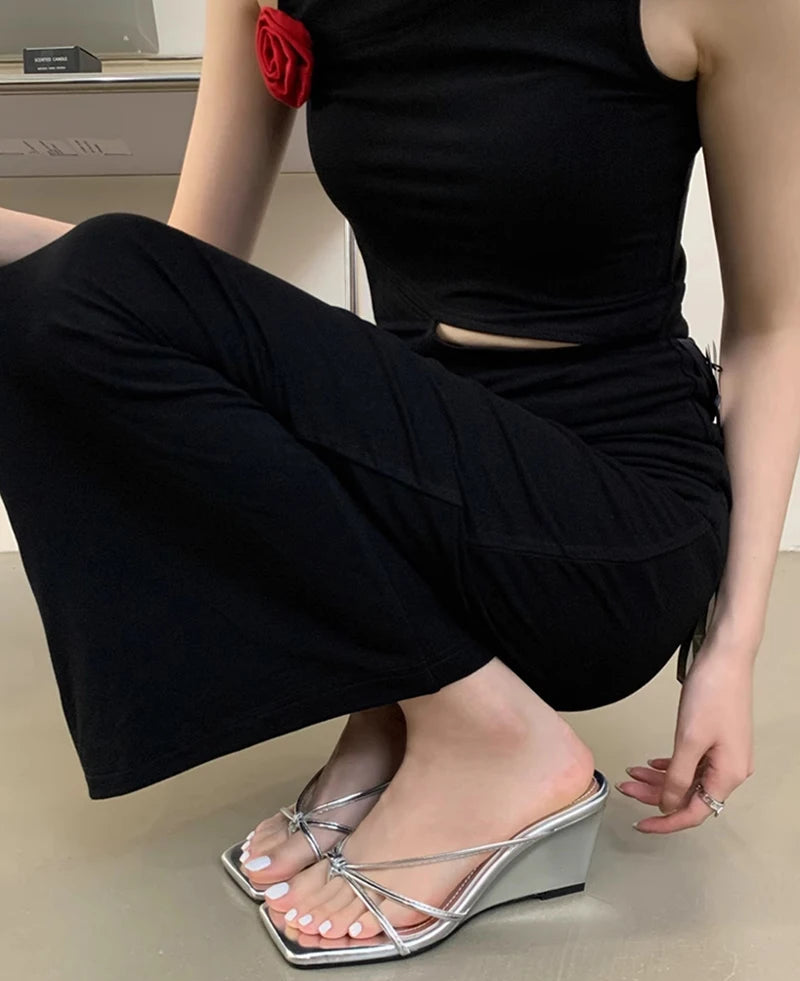 Person wearing black outfit and silver wedge sandals on a neutral background