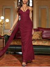 Woman in a burgundy evening gown standing in an elegant room with a couch and lamp.