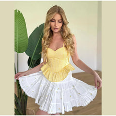 Woman wearing a yellow top and white skirt with ruffled layers, standing indoors.