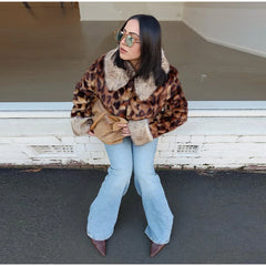 Woman wearing a leopard print coat and light blue jeans sitting on a bench.
