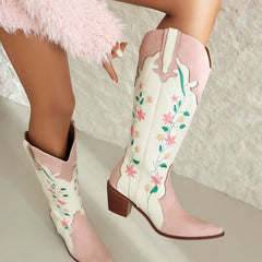 White cowboy boots with pink floral design worn by a person on a light background