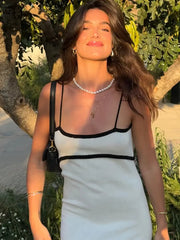 Woman in a white dress with black straps standing outdoors with greenery in the background