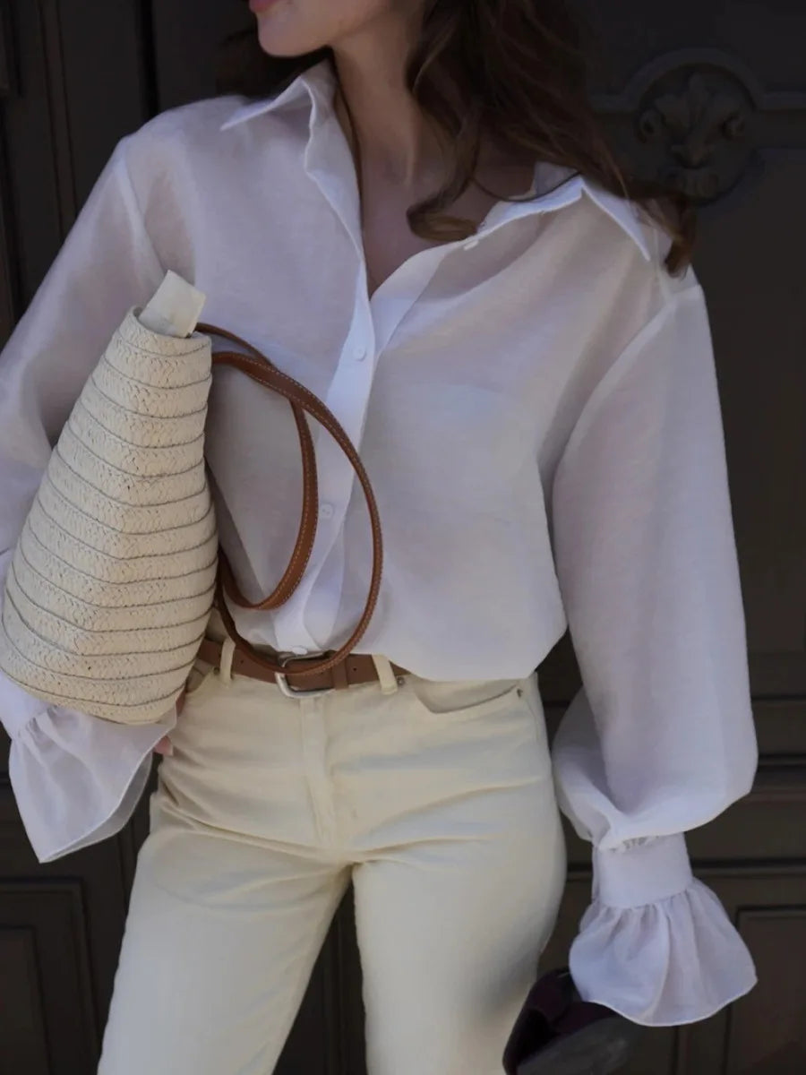 Person wearing a white blouse and beige pants holding a straw bag.
