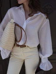 Person wearing a white blouse and beige pants holding a straw bag.