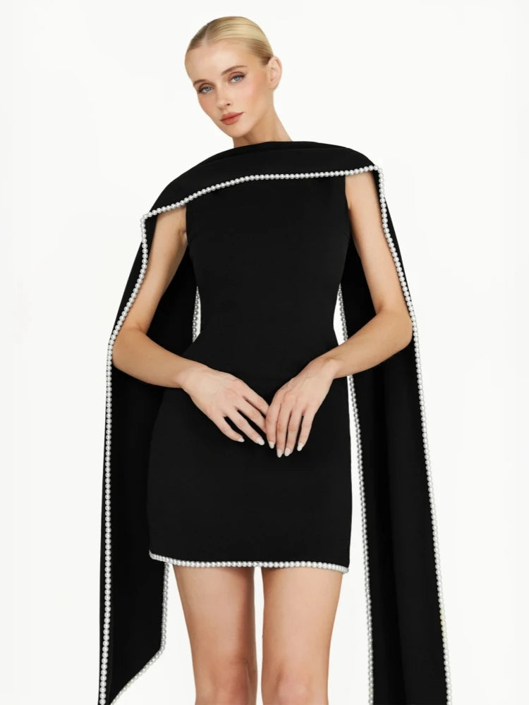 Woman wearing a black dress with a cape and white trim on a white background