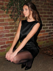 Woman in a black dress sitting against a brick wall