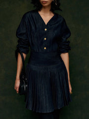 Person wearing a dark blue pleated dress with gold buttons against a dark background