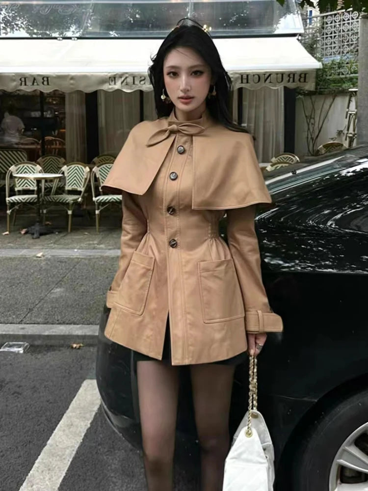 Woman wearing a beige coat with a bow detail in an urban setting.