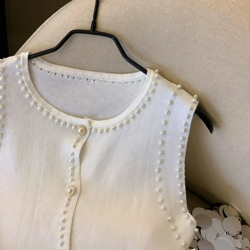 White cardigan with pearl embellishments on a hanger against a neutral background