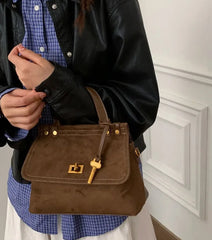 Person holding a brown handbag with a gold clasp against a neutral background