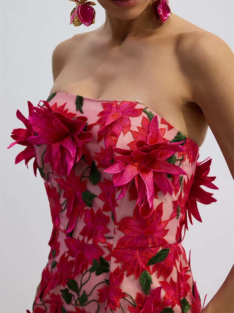 Woman wearing a strapless dress with pink floral embroidery on a plain background