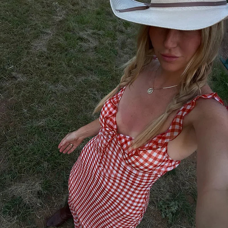 Woman in a red and white checkered dress and white hat sitting on grass