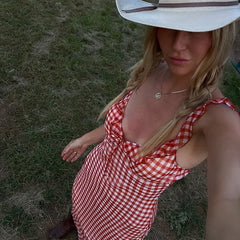 Woman in a red and white checkered dress and white hat sitting on grass