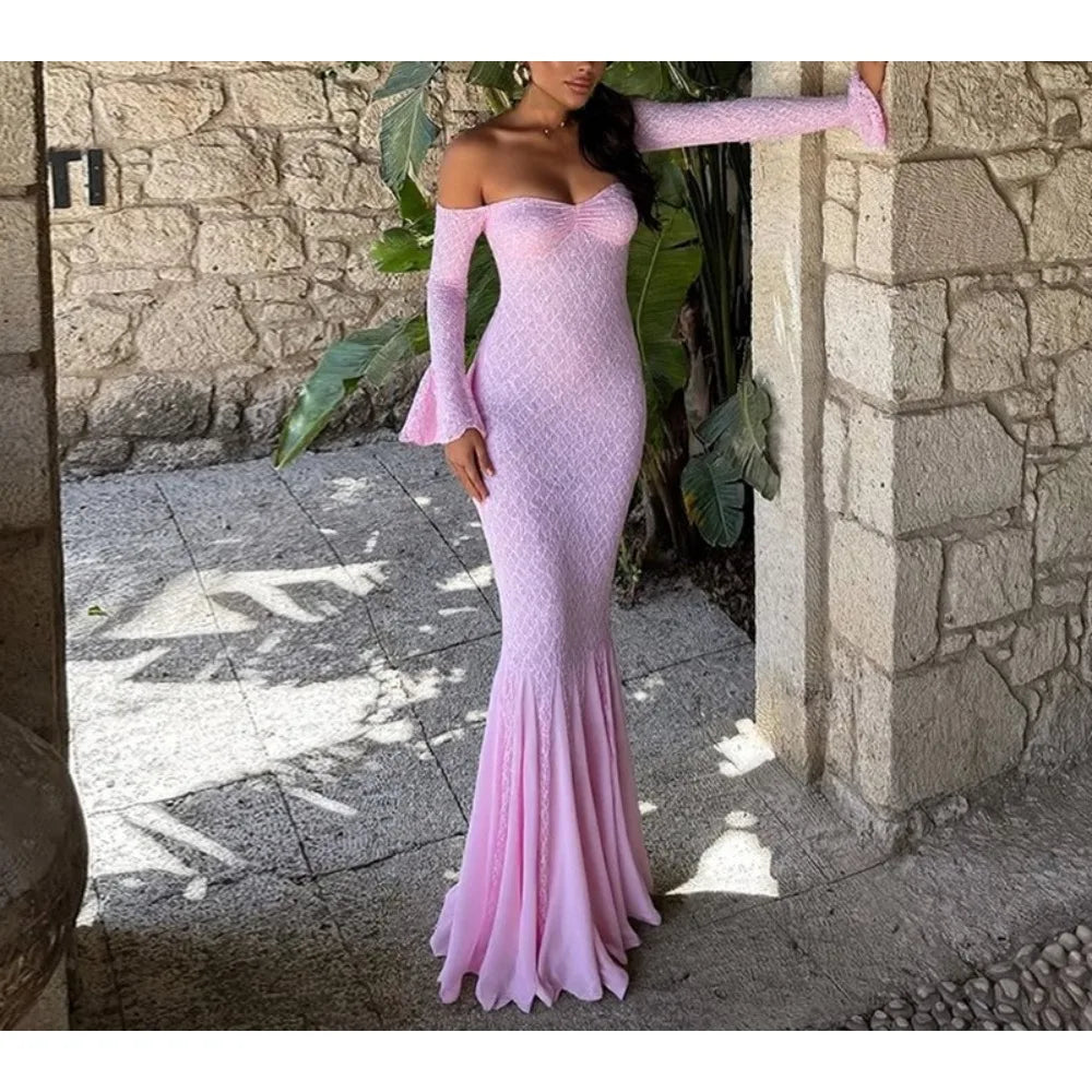 Woman wearing a pink off-shoulder dress standing in front of a stone wall.