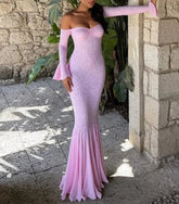 Woman wearing a pink off-shoulder dress standing in front of a stone wall.