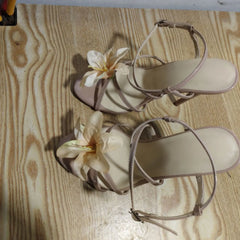 Pair of beige sandals with floral decorations on a wooden surface